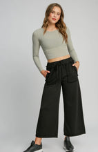 Woman wearing a green long-sleeve crop top and black wide-leg pants on a white background
