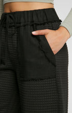 Black textured pants with a hand in the pocket on a white background