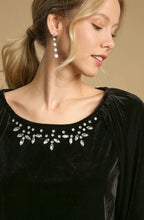 Woman wearing a black dress with a decorative neckline and silver earrings against a beige background