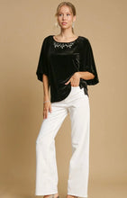 Woman wearing a black blouse with white pants on a beige background