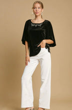 Woman wearing a black top with embellishments and white pants on a beige background