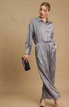 Woman wearing a gray top and pants holding a black clutch against a beige background