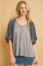 Woman wearing a gray top with sequin sleeves against a beige background