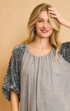 Woman wearing a gray top with sequin sleeves against a beige background