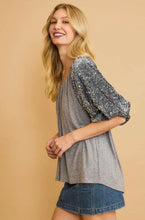 Woman wearing a gray top with sequin sleeves against a beige background