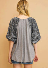 Woman wearing a gray blouse with sequin sleeves on a beige background