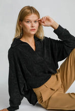 Woman wearing a black sweater and beige pants against a plain background