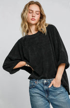 Woman wearing a black oversized sweater and blue jeans against a plain background