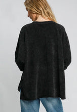 Person wearing a black textured sweater and blue jeans on a plain background