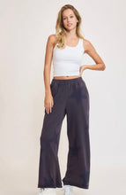 Woman wearing a white tank top and dark blue pants on a light background