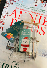 Small bottle with a 'Merry Christmas' tag on top of a book by Annie Rains