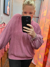 Person wearing a pink sweater taking a selfie in front of a colorful wall.