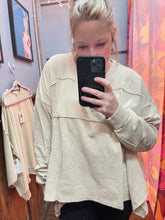 Person wearing a faded khaki oversized sweatshirt holding a phone doing a selfie