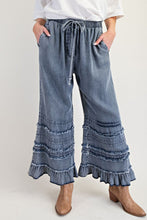 Blue denim wide-leg pants with ruffled bottom hem worn by a person on a white background