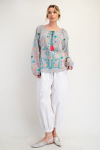 Woman wearing a floral blouse and white pants on a plain background
