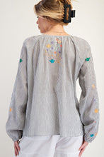 Woman wearing a gray striped blouse with colorful embroidery on a white background