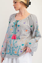 Woman wearing a gray blouse with colorful embroidery and tassels on a white background