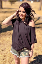 Woman wearing a brown off-shoulder top and camouflage shorts outdoors.