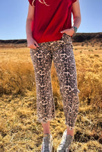 Person wearing red top and leopard print pants standing in a field with blue sky.