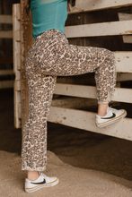 Person wearing leopard print pants and a teal top, standing on a wooden platform.