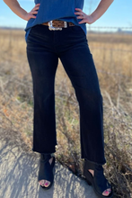 Person wearing black pants and a blue top with a belt, standing in a field.