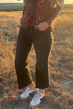 Person wearing a leopard print jacket, black pants, and white sneakers in a field.
