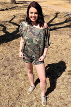 Woman wearing a camouflage outfit standing on grass with trees in the background