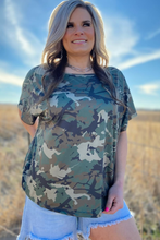 Woman wearing a camouflage shirt with a blue sky and desert landscape in the background