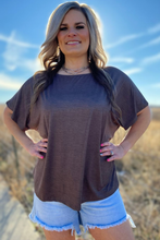 Woman wearing a brown oversized t-shirt and denim shorts standing in a desert landscape.