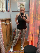Woman taking a mirror selfie wearing a black tank top and patterned pants in a room with colorful curtains.