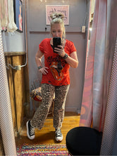 Person taking a mirror selfie wearing an orange t-shirt with a graphic design and patterned pants.