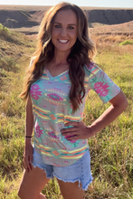 Woman wearing a colorful patterned shirt and denim shorts standing in a grassy field.
