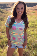 Woman wearing a colorful patterned top and denim shorts standing in a grassy field.