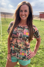 Woman wearing a colorful patterned shirt and shorts standing in a grassy field.