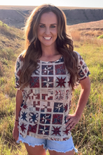 Woman wearing a patterned top and shorts standing in a grassy field.