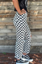 Person wearing black and white checkered pants with a wooden wall background
