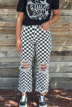 Person wearing a black t-shirt with 'Game Day' design and checkered pants against a wooden wall.